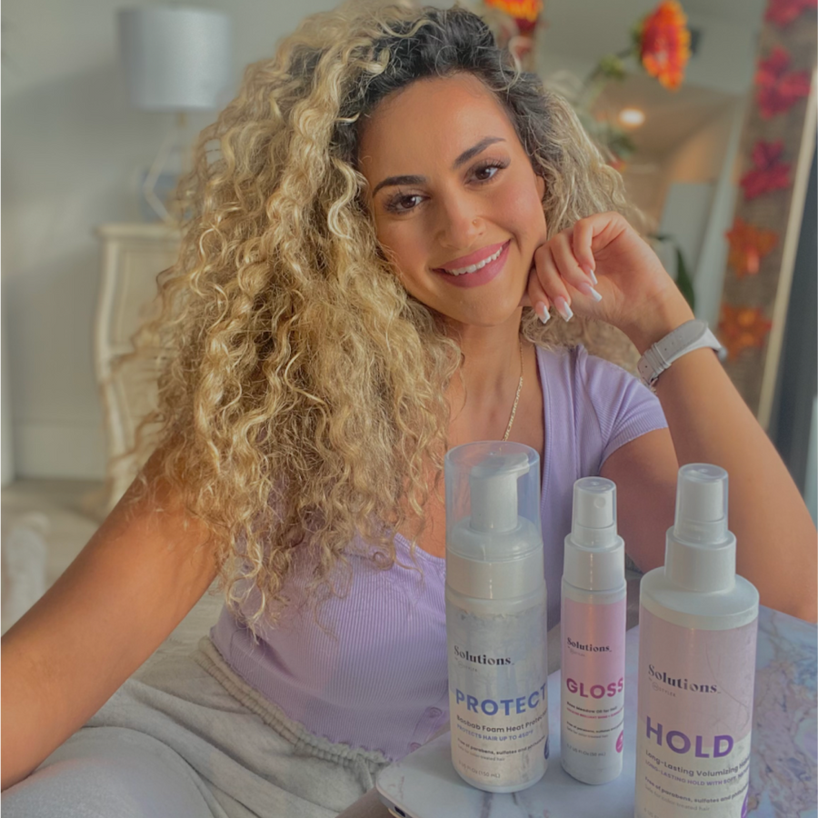 Model with curly blonde hair next to bottle of GLOSS Rose Meadow Hair Oil-InStyler