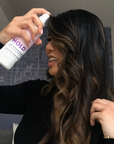 Photo of model with curly brown hair spraying her hair with HOLD Volumizing  Hair Spray-InStyler